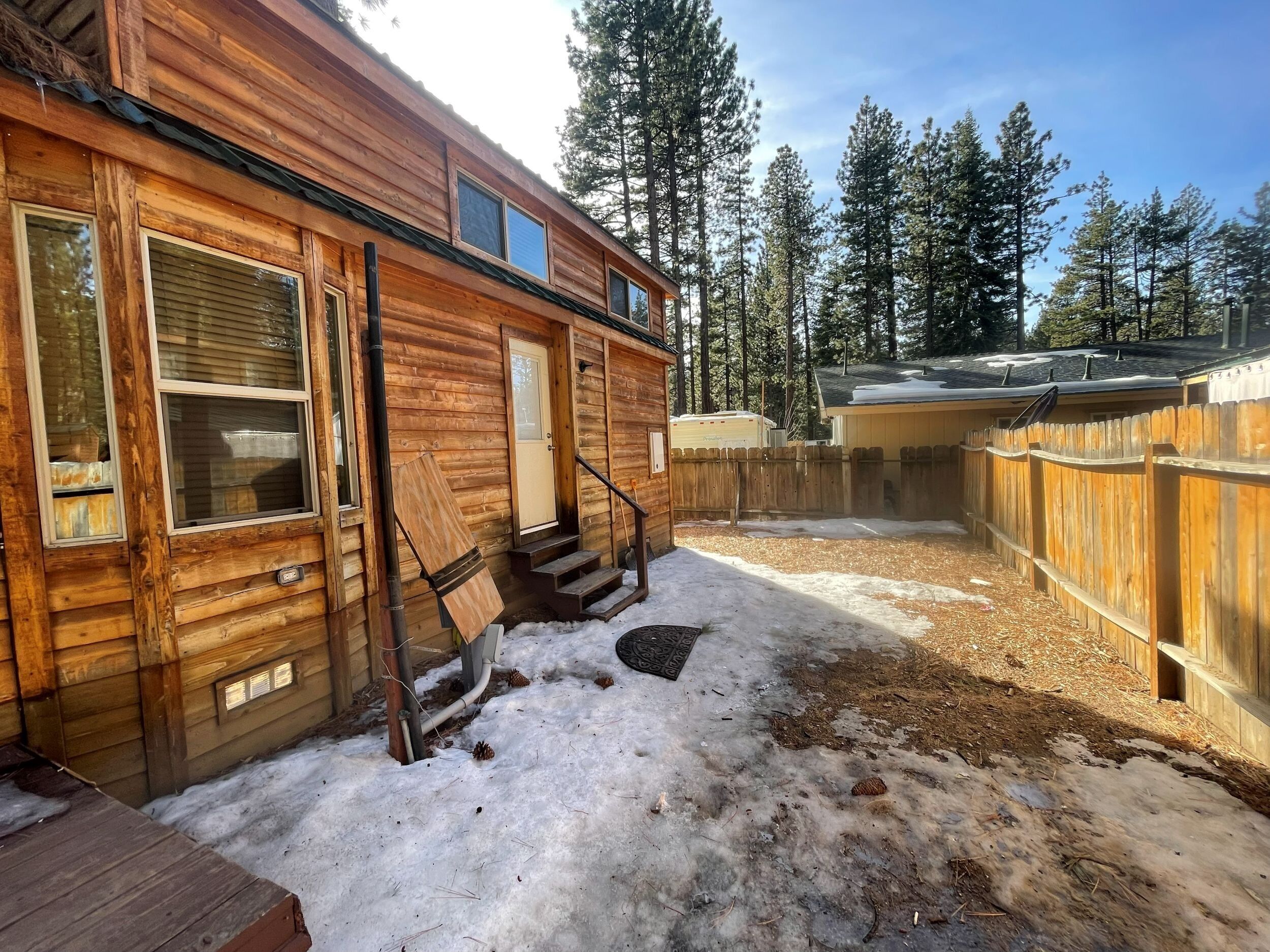 A wooden cabin with a porch, steps leading to a door, and a fenced yard.