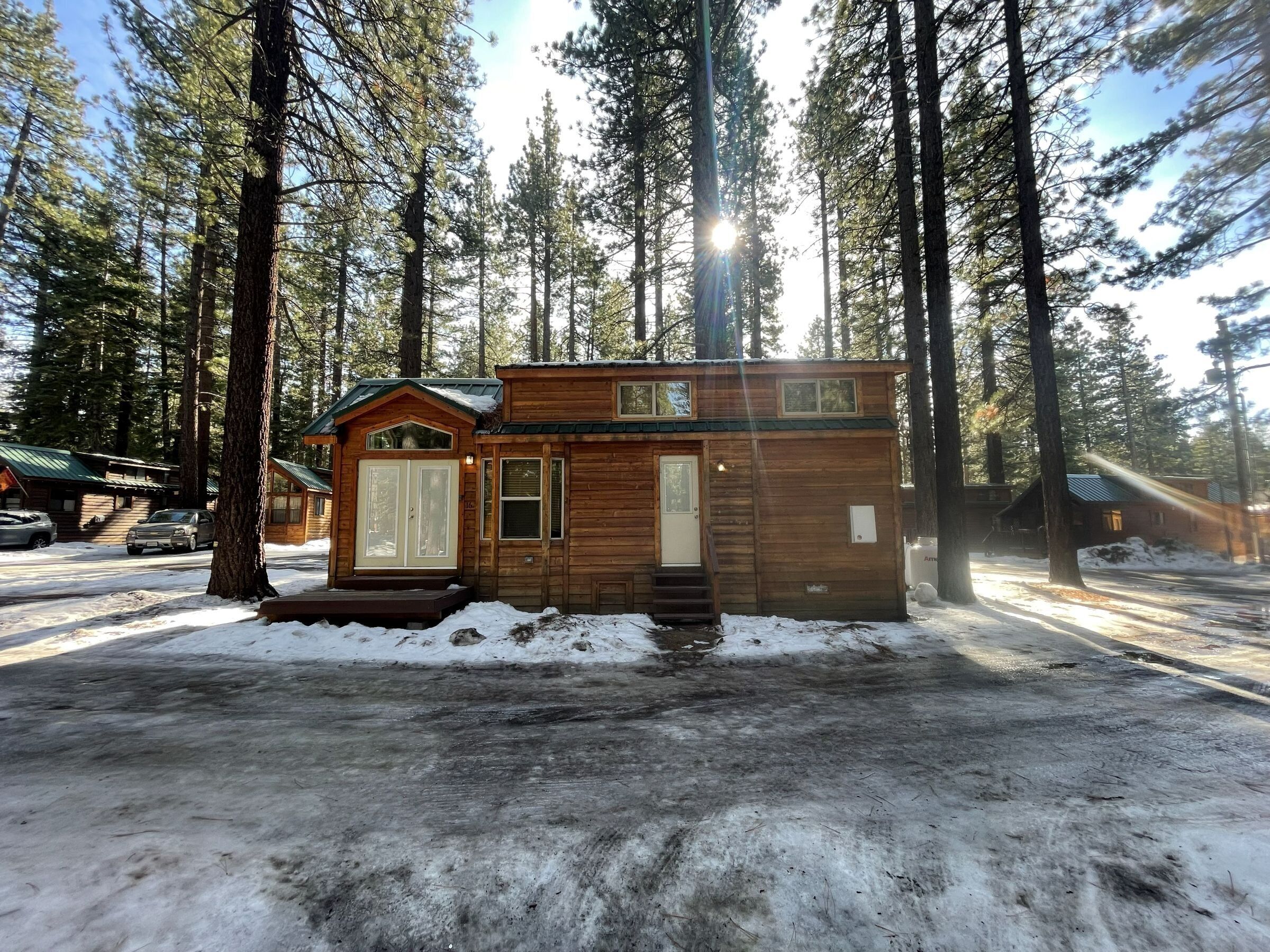 A small cabin with a front porch, a garage, and a covered driveway.