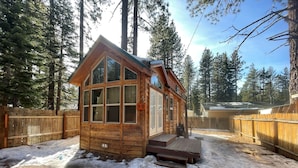 A wooden cabin with large windows, a deck, and a fenced yard in a forested area. - Wooded Cabin Perfect for South Lake Tahoe Day Trips (El Dorado County)