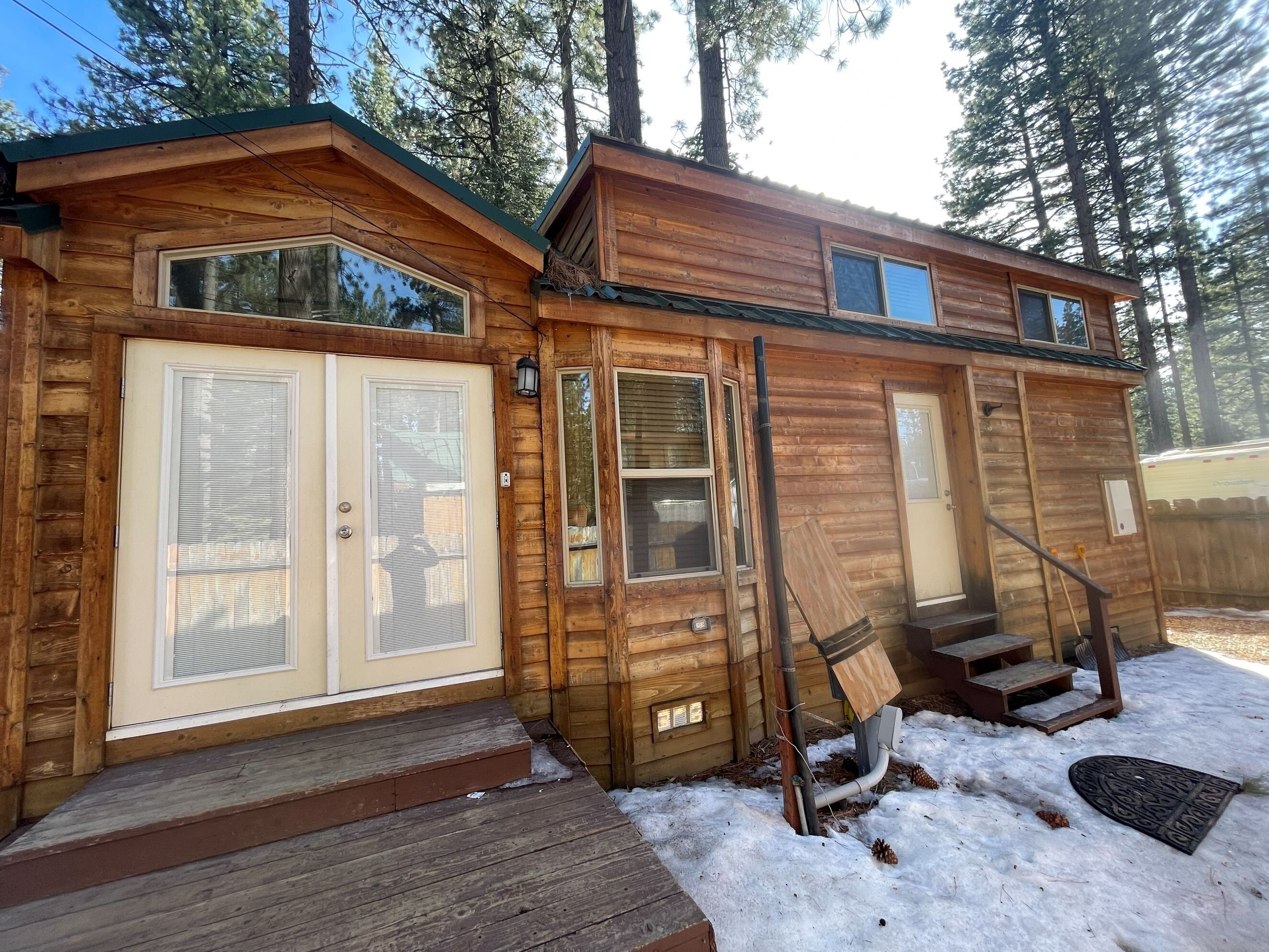 A wooden cabin with a front door, a set of stairs leading to a deck, and a small porch area.