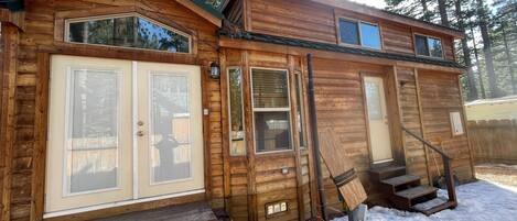 A wooden cabin with a front door, a set of stairs leading to a deck, and a small porch area.