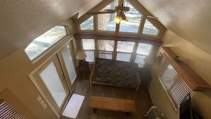 A loft-style room with a sloped ceiling, large windows, a ceiling fan, a bench, and a radiator. - Wooded Cabin Perfect for South Lake Tahoe Day Trips (El Dorado County)