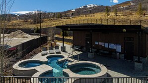 Un área de piscina con dos jacuzzis, una zona de estar techada y un edificio con señal de salida.
