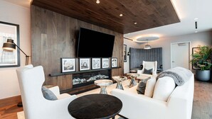 Una sala de estar moderna con un sofá, sillones, una mesa de centro, un televisor de pantalla plana montado en una pared de madera, cuadros enmarcados y una planta en maceta.