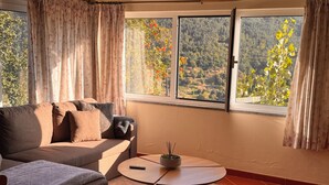 A living room with a sofa, a small table, and a view of a forested area through a window.