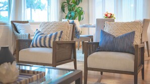 Un salón acogedor con sillones de mimbre, una mesa de centro de vidrio y un ventanal con cortinas.