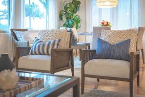 A cozy living room with wicker chairs, a glass coffee table, and a large window with curtains. - La Jolla Shores! Beach Across Street+Walk Everywhere (San Diego)