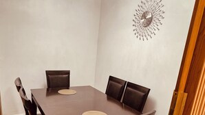 A dining room with a rectangular table, six chairs, a chandelier, and a wall clock.