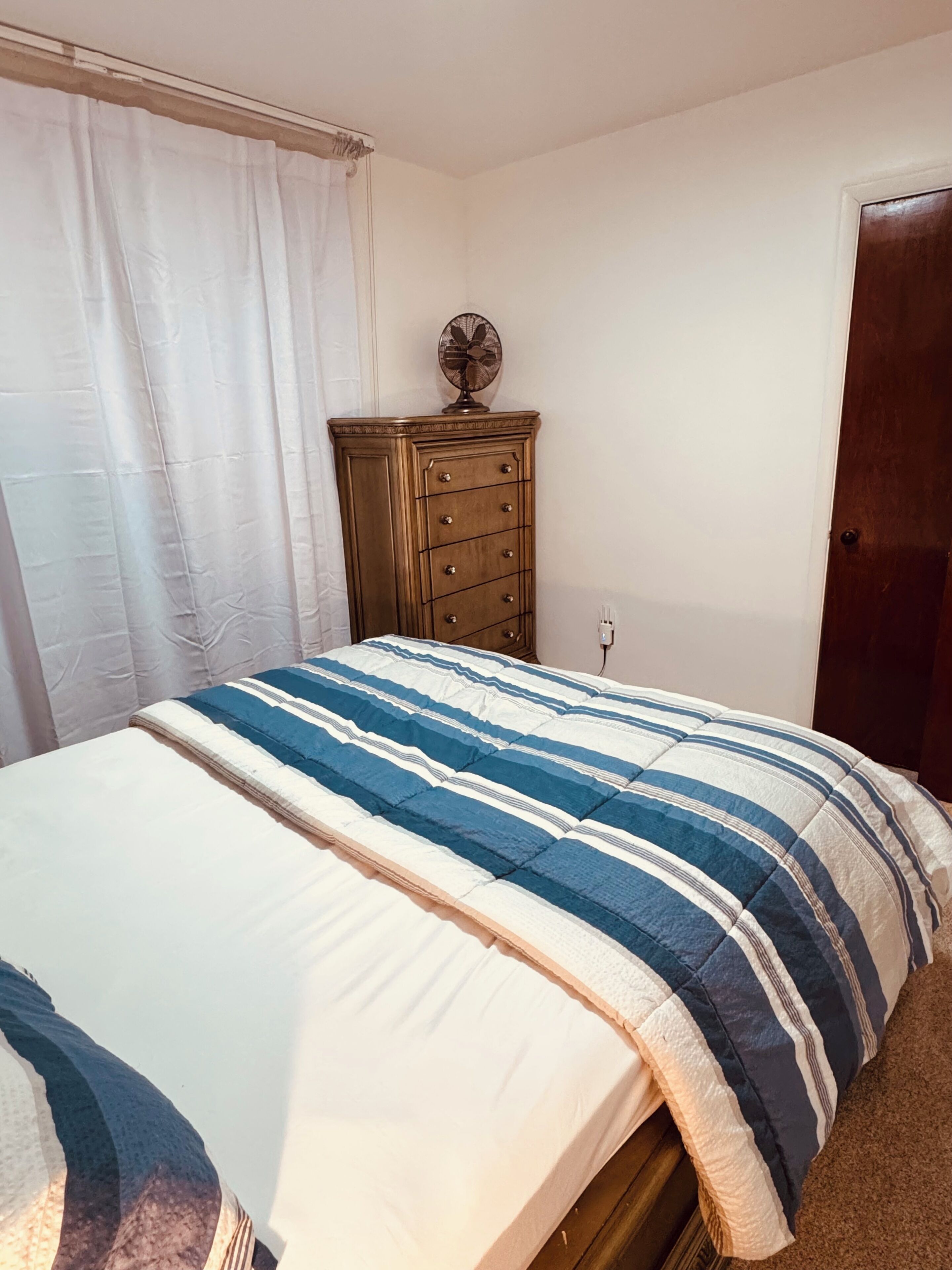 Un dormitorio con cama, cómoda, ventilador y puerta.
