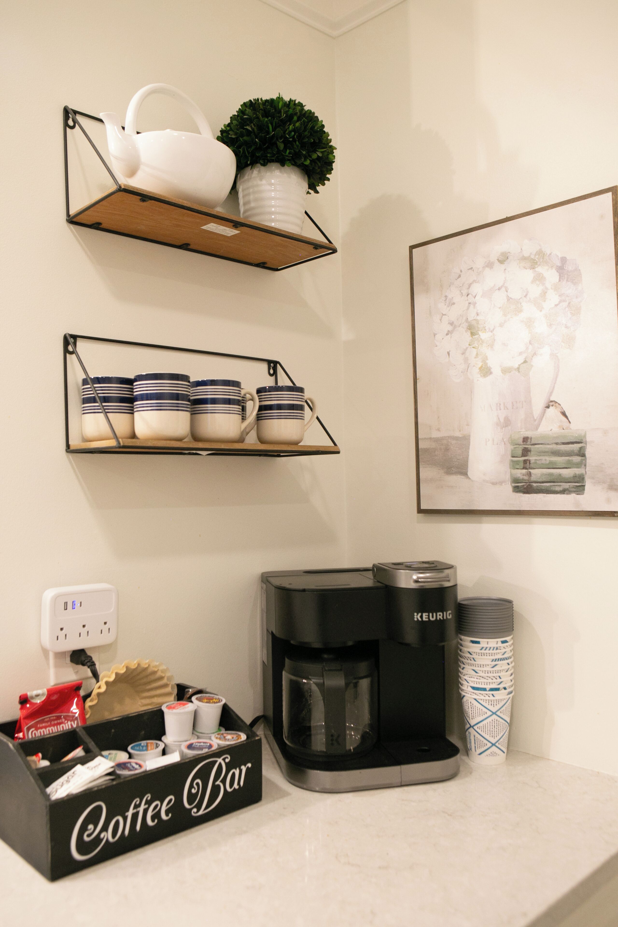 A coffee bar setup with a Keurig machine, mugs, and a tray of coffee pods.
