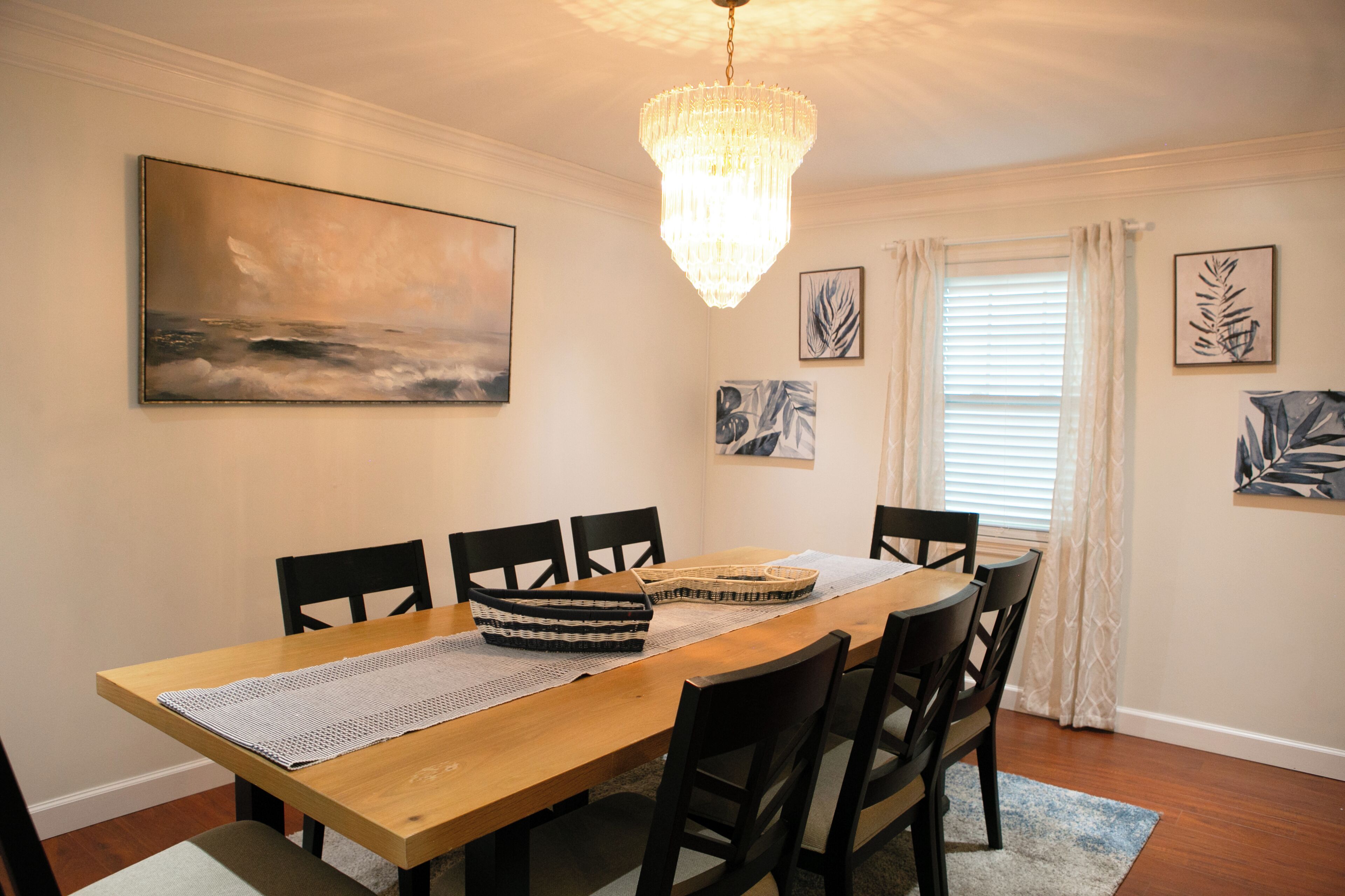 Ein Esszimmer mit Holztisch, schwarzen Stühlen, einer Chandelieber und Bildern an den Wänden.