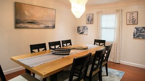 Ein Esszimmer mit Holztisch, schwarzen Stühlen, einer Chandelieber und Bildern an den Wänden.