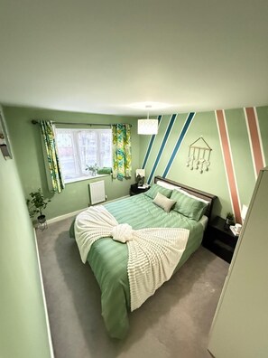 Un dormitorio con cama, ventana, mesita de noche y un adorno en la pared.