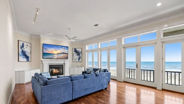 A spacious living room with a fireplace, a large sofa, and a view of the ocean through large windows. - Beachfront 5BR | Hot Tub & Fire Pit | Game Room (Galveston)