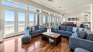 A spacious living room with large windows, a ceiling fan, and a view of the beach. - Beachfront 5BR | Hot Tub & Fire Pit | Game Room (Galveston)