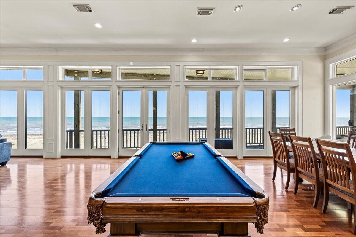Une table de billard dans une pièce dotée de grandes fenêtres donnant sur la plage.