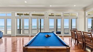 Une table de billard dans une pièce dotée de grandes fenêtres donnant sur la plage.