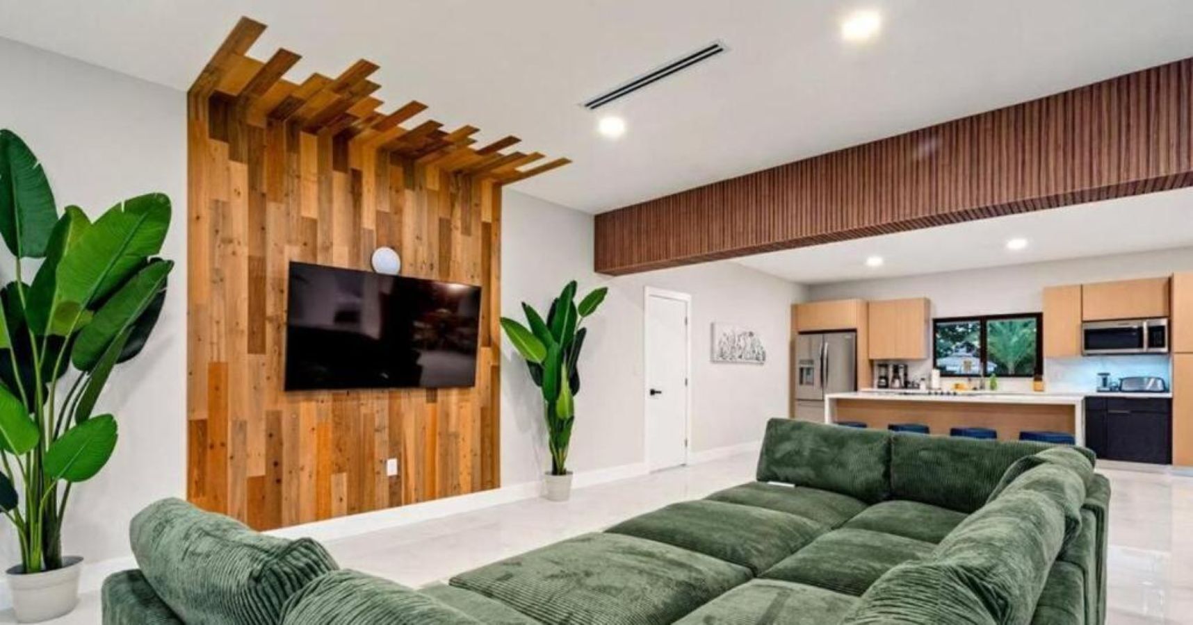 A modern living room with a wooden accent wall, a flat-screen TV, and a green sofa.