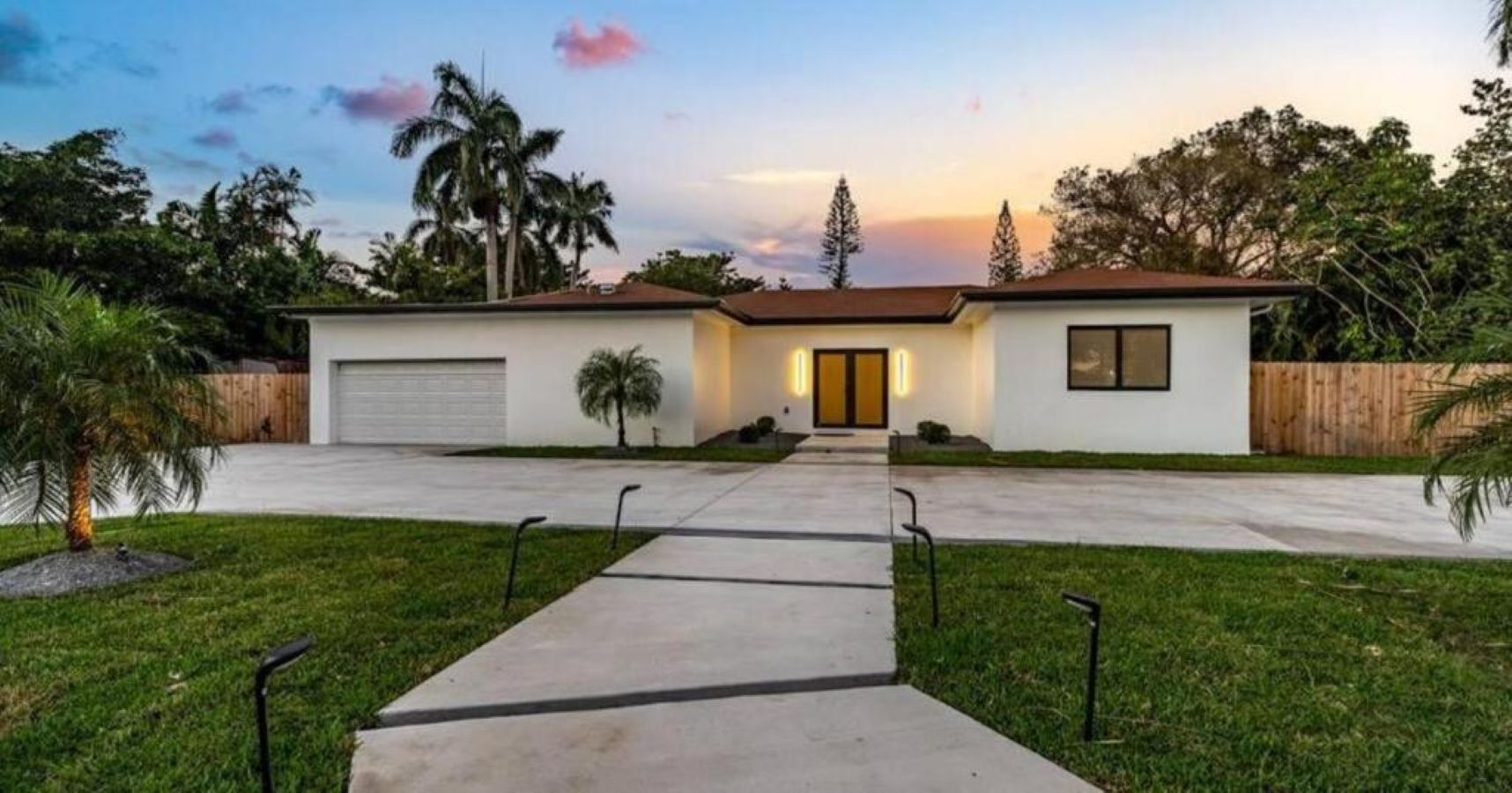 A two-story house with a garage, a front yard with a pathway, and a sunset in the background.