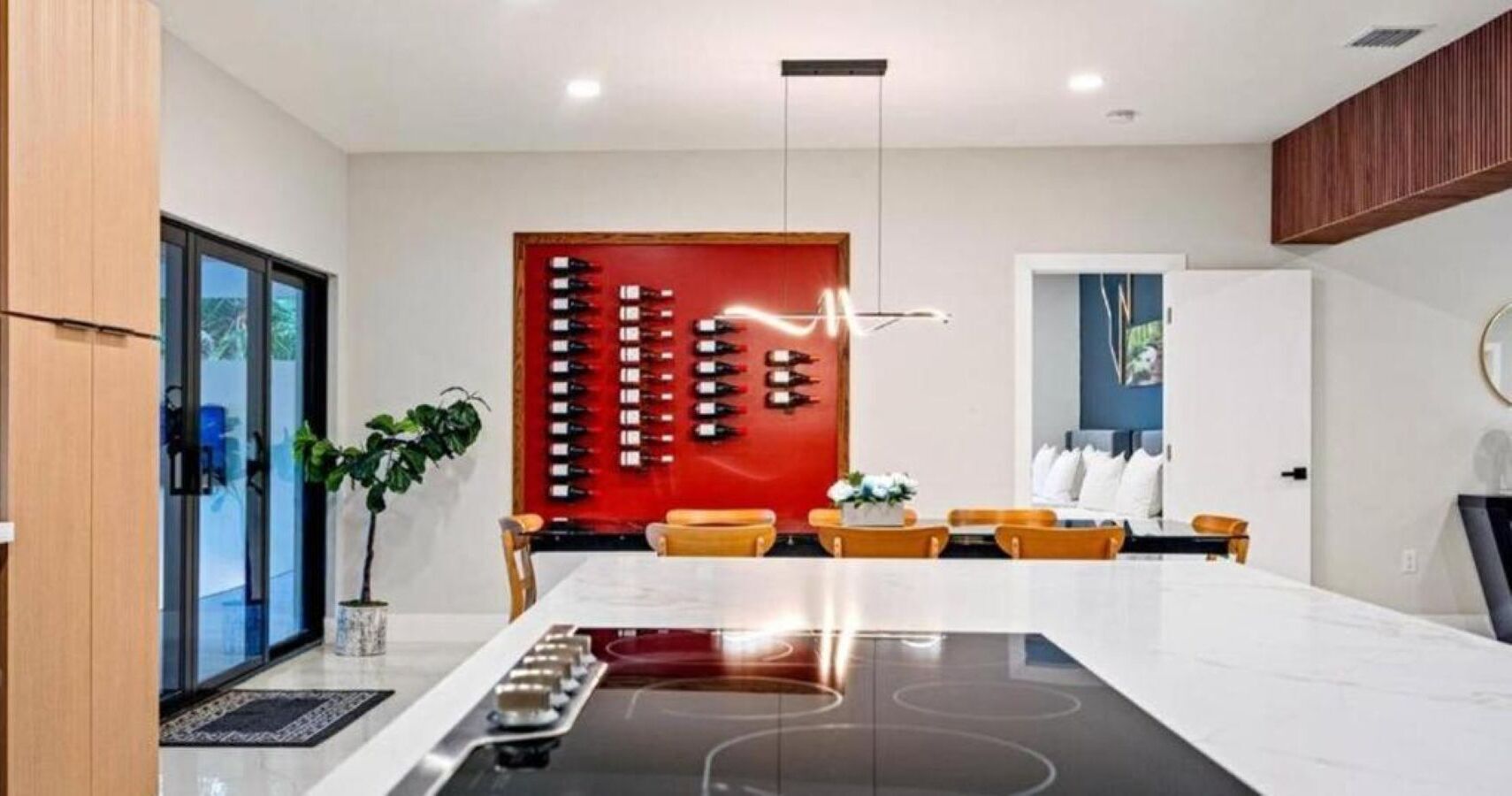 A modern kitchen with a central island, a red wine wall, and a dining area with yellow chairs.