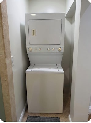 A compact, white laundry room with a front-loading washer and dryer, a small window, and a door leading to another room.