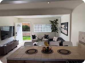 A living room with a TV, sofa, coffee table, and a dining area with a tiled table.