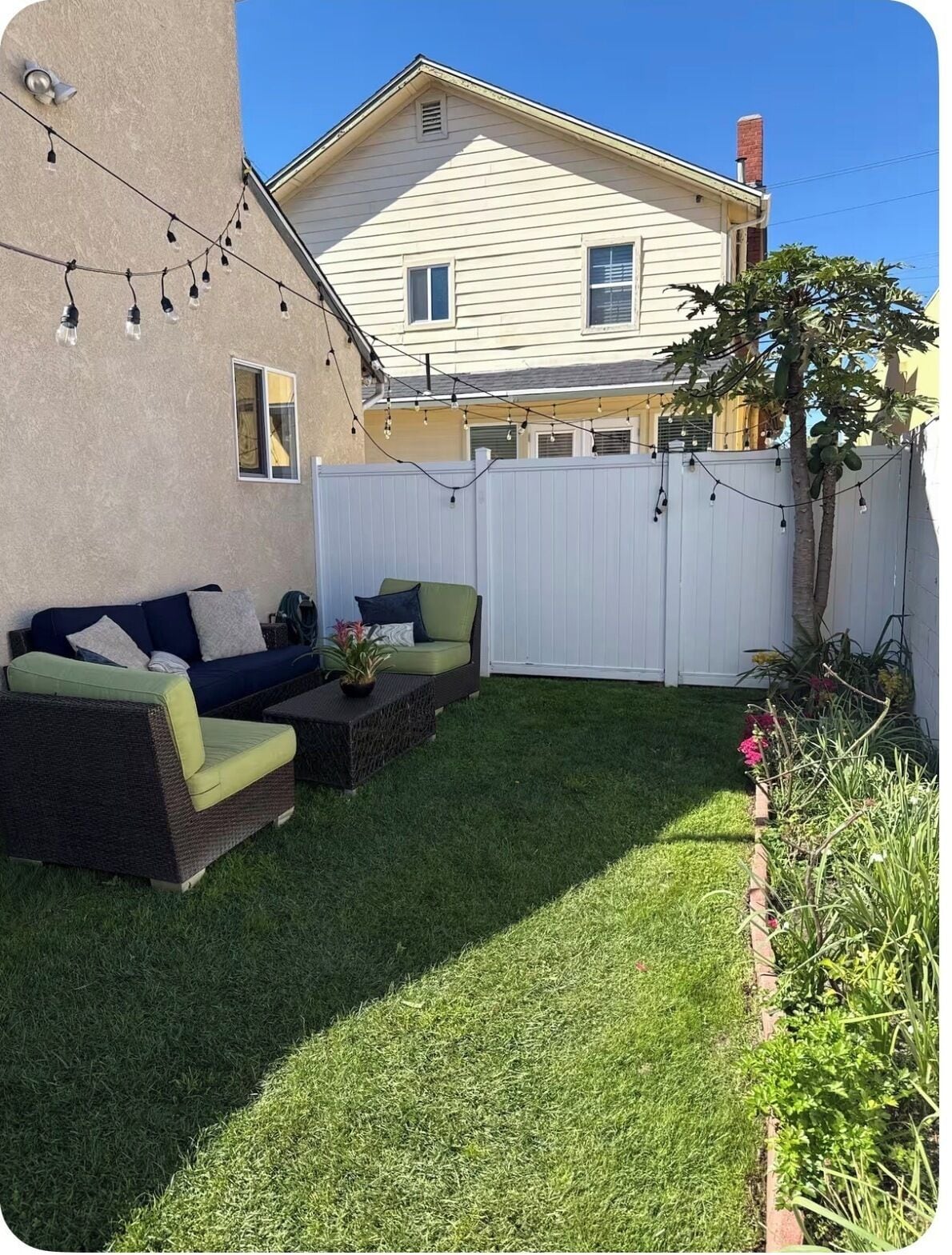 A backyard with a white fence, a lawn, and two outdoor sofas.
