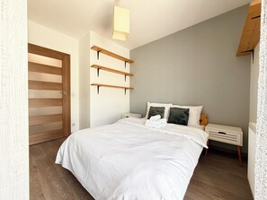 Une chambre à coucher avec un lit, des tables de chevet, une porte en bois et un luminaire au plafond.