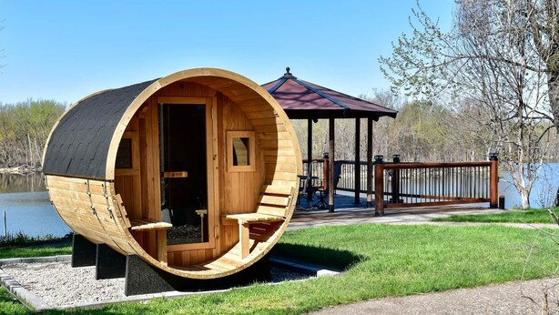 A wooden barrel-shaped structure with a deck and a gazebo in the background.