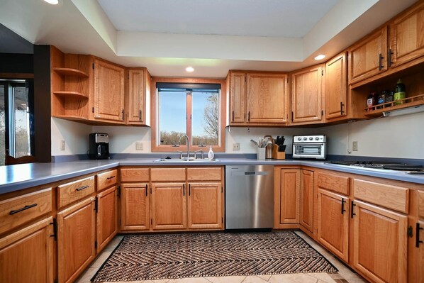A modern kitchen with wooden cabinets, a stainless steel dishwasher, a built-in oven, and a window above the sink.