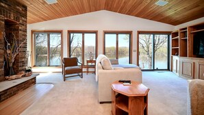 A spacious living room with a high ceiling, large windows, a fireplace, and a television.