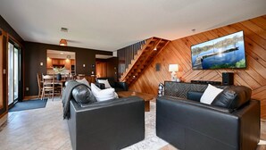 A modern living room with a TV, leather sofas, a dining area, and a staircase.