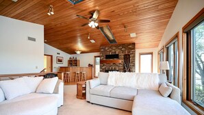 A modern living room with a wooden ceiling, a large sofa, a fireplace, and a dining area.