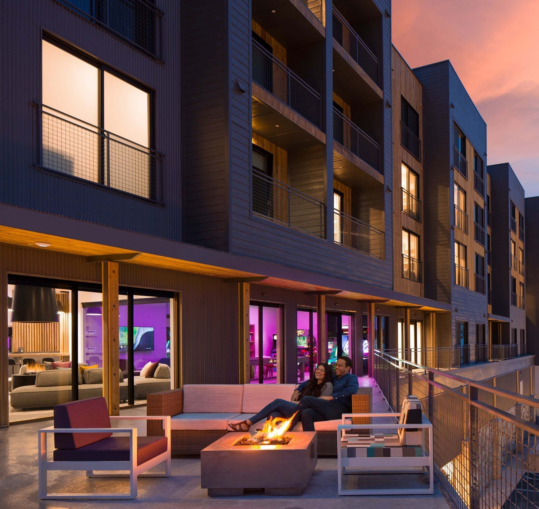 A modern building with a rooftop lounge area featuring outdoor seating and a fire feature.