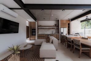 A modern kitchen with built-in appliances, a dining area with a wooden table and chairs, and a living room with a sofa and a TV mounted on the wall. - The Town Praia 38 (Puntarenas)