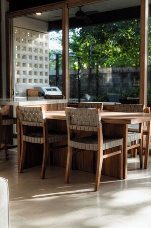 Un espace repas avec une table et des chaises en bois, de grandes fenêtres et une vue sur la verdure environnante.
