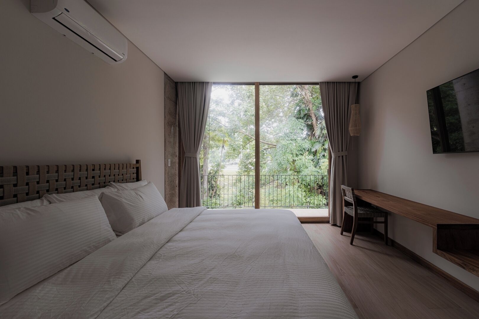 Ein Schlafzimmer mit einem großen Bett, einem Schreibtisch und einem Balkon mit Blick auf Grünflächen.