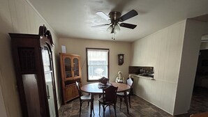 A dining area with a round table, chairs, a cabinet, a ceiling fan, and a window with blinds. - Lakeside Retreat: Peaceful Jordan Lake Getaway (New Hill)