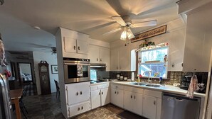 A kitchen with white cabinets, a built-in oven, a dishwasher, and a ceiling fan. - Lakeside Retreat: Peaceful Jordan Lake Getaway (New Hill)