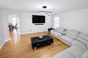 Ein modernes Wohnzimmer mit einer Couch, einem Couchtisch, einem Fernseher und einem Essbereich im Hintergrund.