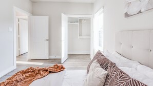 Ein Schlafzimmer mit einem Bett, einem großen Fenster und einer Tür zu einem anderen Raum.