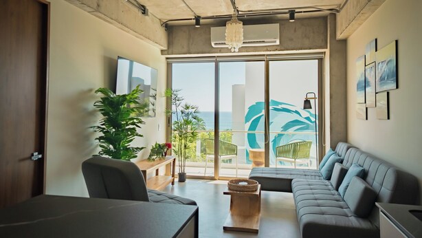 Ein modernes Wohnzimmer mit einem großen Sofa, einem Esstisch und Meerblick durch große Fenster.