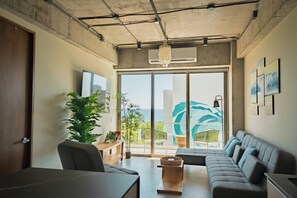 Una sala de estar moderna con un sofá grande, una mesa de comedor y vistas al océano a través de amplios ventanales.