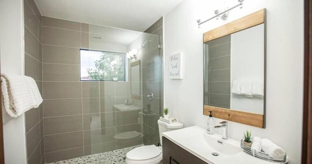 Une salle de bain moderne avec une douche à l’italienne en verre, un lavabo blanc et un grand miroir.
