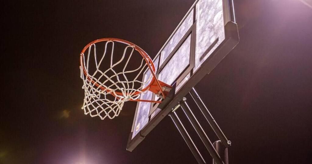 Un aro de baloncesto con red, sujeto a una estructura metálica, sobre un fondo oscuro.