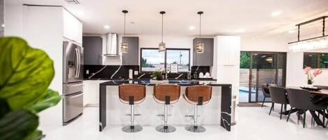A modern kitchen with a central island, bar stools, and a dining area with chairs.
