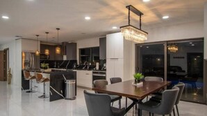 A modern kitchen with a dining area, large windows, and a chandelier. - Villa Dubai by Glam Homes (Ojus)