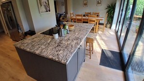 A modern kitchen with a granite countertop, wooden chairs, and a dining table. - Spacious 3BR Home with Garden and Parking (Southampton)