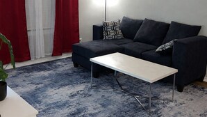 A living room with a sofa, a coffee table, a red and white curtain, a painting on the wall, and a floor lamp. - Cozy & Comfortable in walking distance to AT&T, near Sixflags (Arlington)