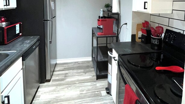 A compact kitchen with stainless steel appliances, a clock on the wall, and a small island with a red appliance. - Cozy & Comfortable in walking distance to AT&T, near Sixflags (Arlington)